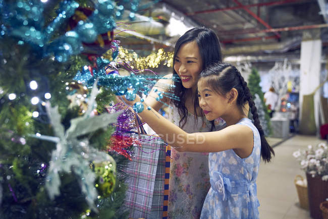 Young asian woman and girl looking at christmas tree decoratons — Stock Photo
