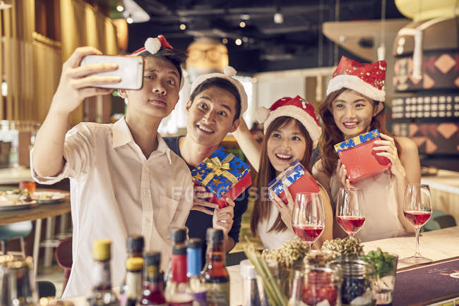 Heureux jeunes amis asiatiques célébrer Noël ensemble dans café et prendre selfie — Photo de stock