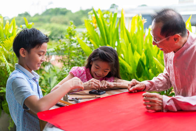 Happy asian family together, grandfather and grandchildren drawing hieroglyphs — Stock Photo
