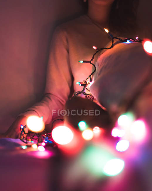 Imagen recortada de la mujer relajándose en casa con guirnalda de Navidad - foto de stock
