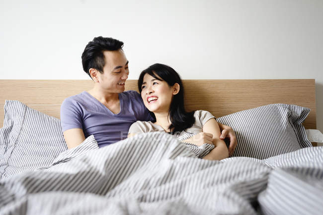 Взрослая азиатская пара, лежащая в постели дома — стоковое фото