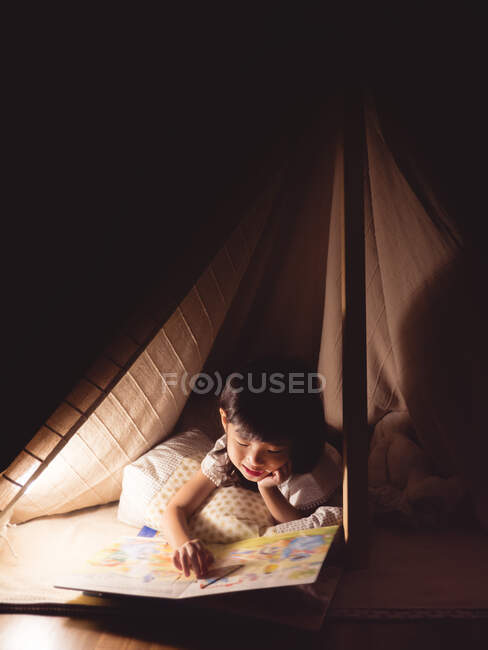 Menina bonito está lendo um livro na tenda — Fotografia de Stock