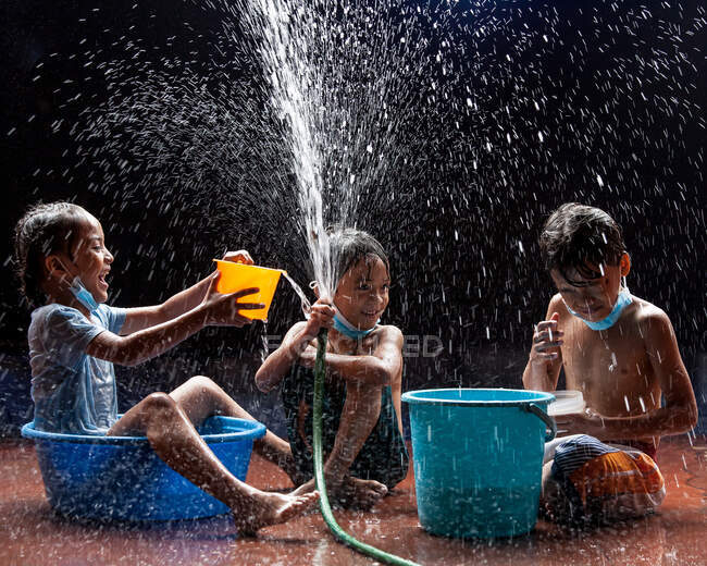 Três amigos desfrutando sob uma mangueira de água — Fotografia de Stock