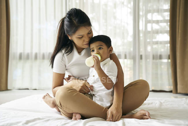 Ásia mãe relógios como ela filho alimenta no leite garrafa — Fotografia de Stock