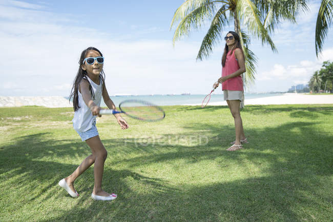 Young asian mother with cute daughter playing in badminton outdoors — Stock Photo
