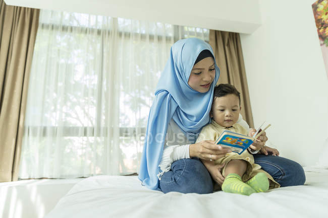 Молодая азиатская мусульманка мать и ребенок reding книги дома — стоковое фото