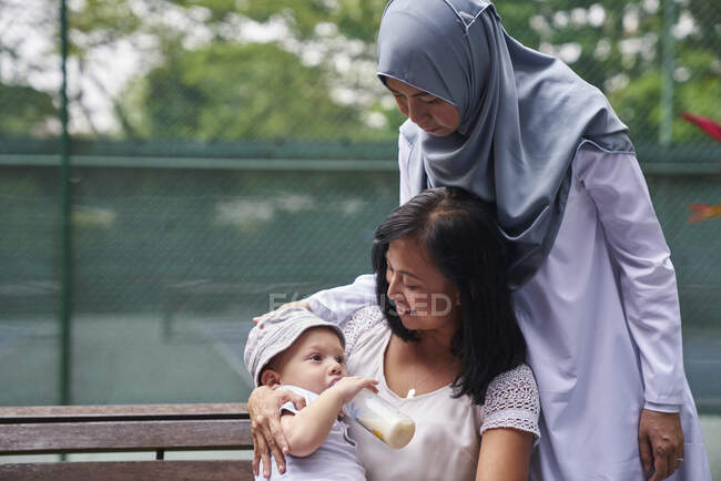Mother and Grandmother feeding their son milk at a park — Stock Photo