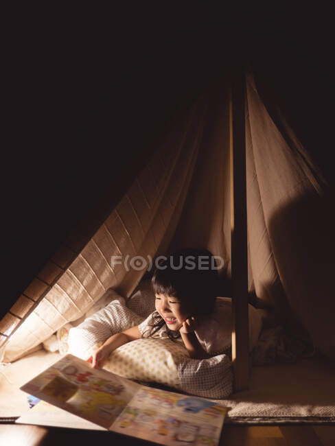 Petite fille mignonne lit un livre dans la tente — Photo de stock