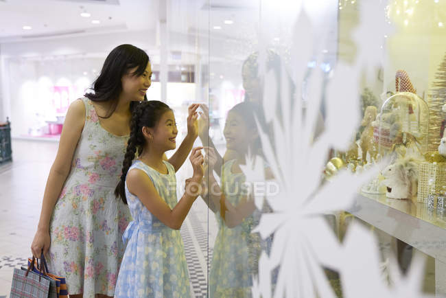 Joven asiático mujer y chica mirando a través de vidrio en mall - foto de stock