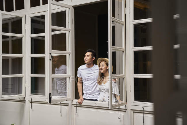 Feliz jovem asiático casal olhando para fora da janela — Fotografia de Stock