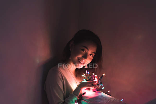 Jeune femme asiatique relaxant à la maison avec guirlande de Noël — Photo de stock