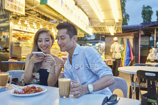 Happy young asian couple sitting together in street cafe — Stock Photo