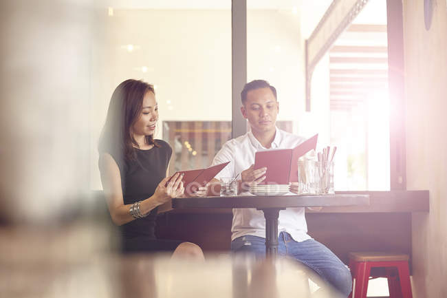 Young attractive asian couple having date in cafe, watching at menu — Stock Photo