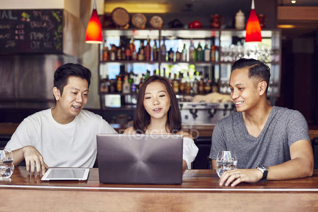Heureux jeunes amis asiatiques ensemble travailler avec ordinateur portable dans bar — Photo de stock