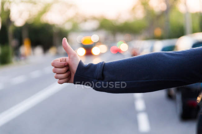Cropped image of female hand showing hitchhiking sign — Stock Photo
