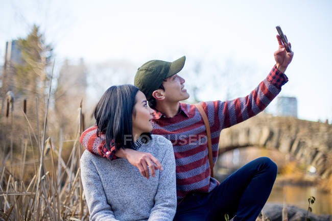 Atractiva pareja de turistas juntos tomando selfie en parque - foto de stock