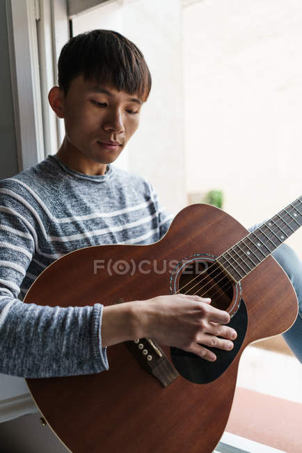 Молодий дорослий азіатський чоловік грає на гітарі вдома — стокове фото