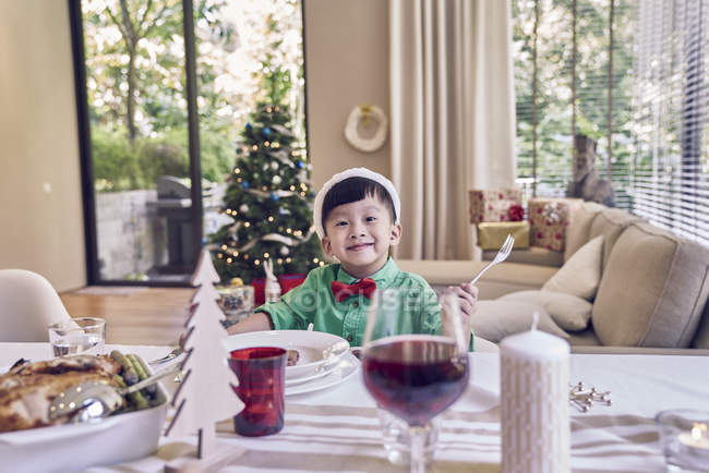 Little asian boy sitting at christmas table and smiling — Stock Photo