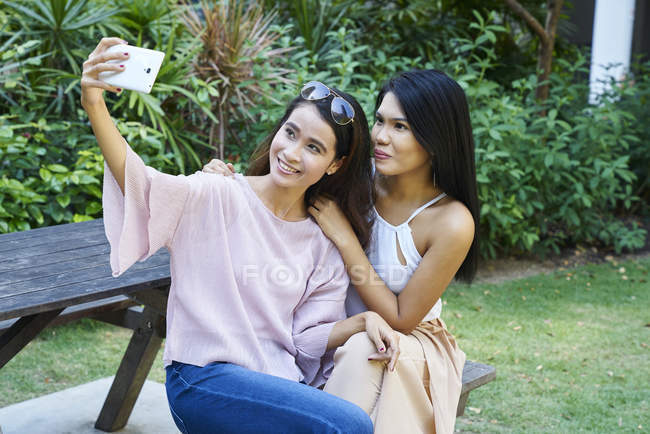 Junge malaiische Frauen machen ein Selfie auf einer Holzbank — Stockfoto