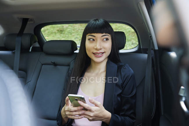 Femme d'affaires utilisant son mobile sur le siège arrière d'une voiture — Photo de stock