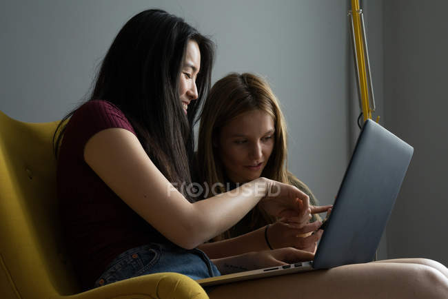 Mulher chinesa com um amigo e laptop se divertindo em uma poltrona amarela . — Fotografia de Stock