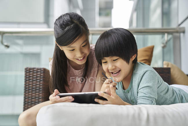 Happy young asian boy and girl together using digital tablet at home — Stock Photo