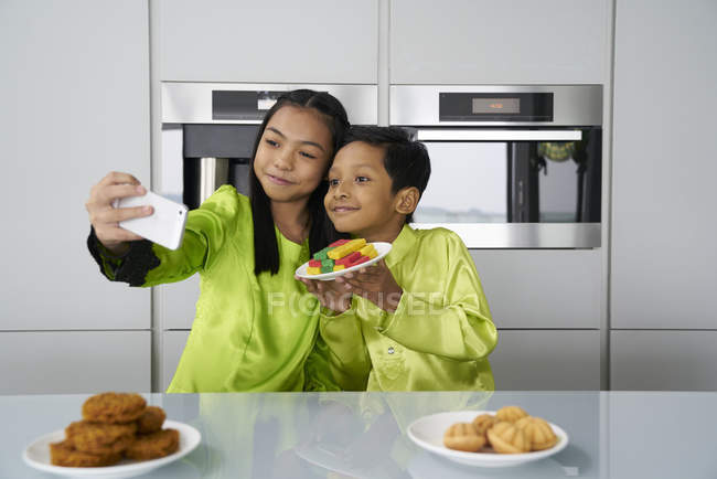 Junge asiatische Geschwister feiern Hari Raya zusammen zu Hause und machen Selfie mit Süßigkeiten — Stockfoto