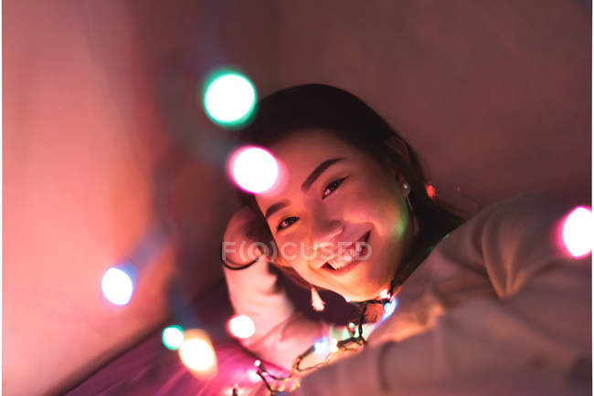 Junge Asiatin entspannt zu Hause mit Weihnachtsgirlanden — Stockfoto