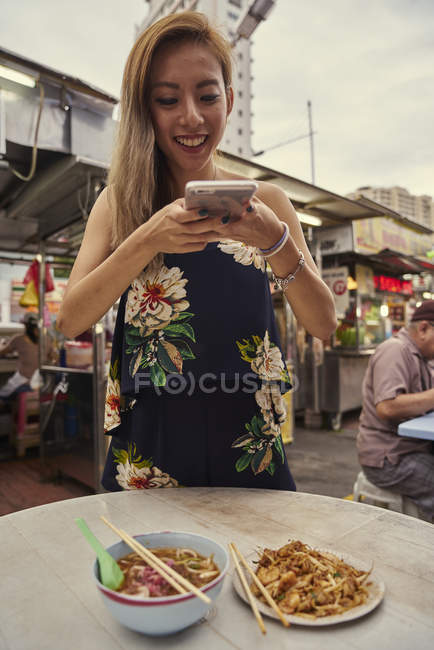Молода азіатка фотографує їжу на столі у вуличному кафе — стокове фото