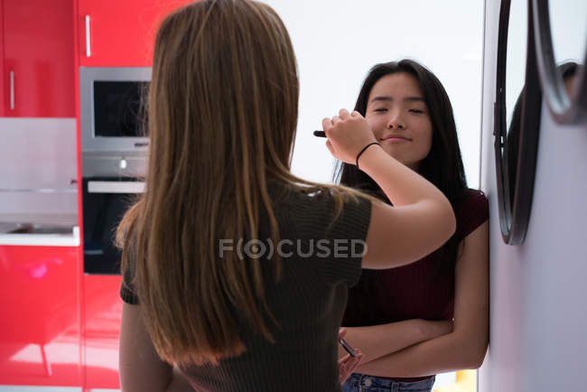 Молодая женщина помогает подруге гримировать лица — стоковое фото