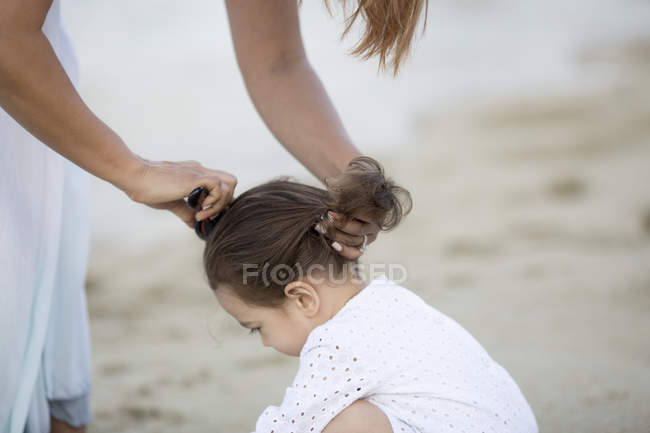 Mother making hairdo to daughter on beach — Stock Photo