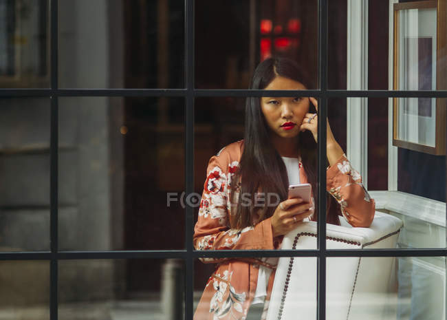 Довольно длинные волосы китаянка с помощью смартфона через окно — стоковое фото