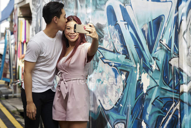 Young attractive asian couple taking selfie against graffiti — Stock Photo