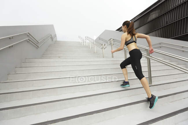 A young asian, female runner is running up a staircase in Singapore. — Stock Photo