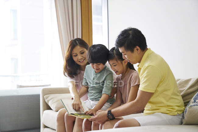 Счастливая молодая семья вместе читает книгу в спальне — стоковое фото