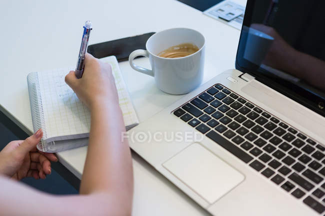 Cropped image of woman working with laptop and notebook in modern office — Stock Photo