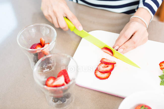 Immagine ritagliata di donna che taglia fragole a casa — Foto stock
