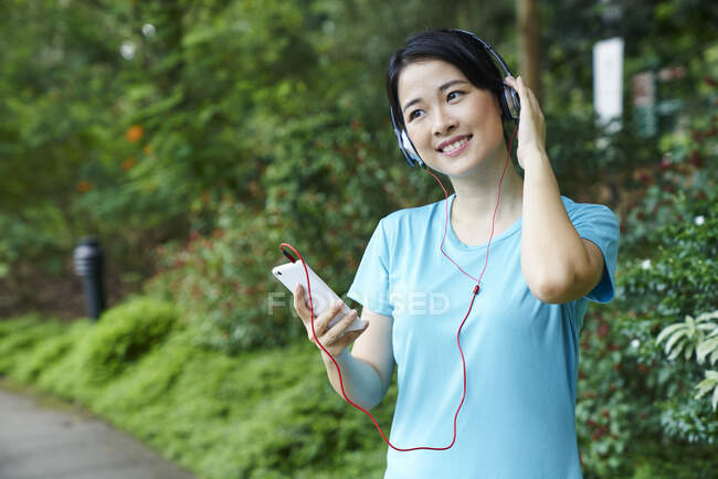 Porträt einer Frau, die beim Spazierengehen im botanischen Garten Musik hört — Stockfoto