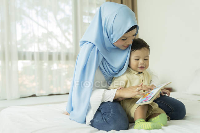 Young asian muslim mother and child reding book at home — Stock Photo