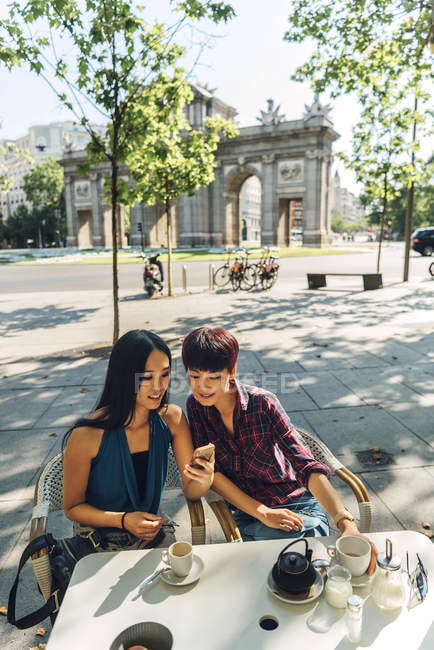 Japanese and Chinese female tourists having coffee in terrace close to Puerta de Alcala in Madrid, Spain. — Stock Photo