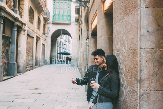 Молодая азиатская пара пьет кофе на улице и смотрит на мобильный телефон — стоковое фото