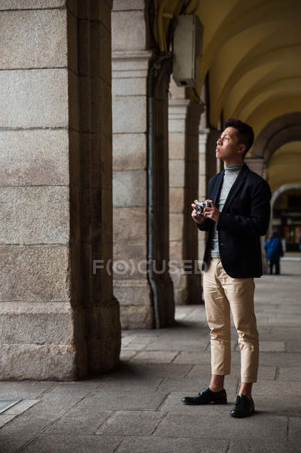 Hombre chino joven casual tomando fotos con una cámara de fotos vintage en Madrid, España - foto de stock