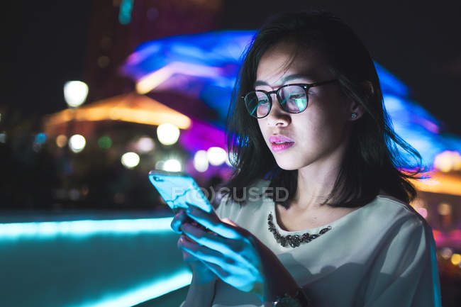 Junge Frau mit ihrem Handy auf der Straße, nachts Licht Hintergrund — Stockfoto