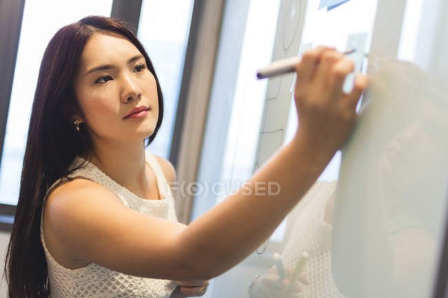 Jovem mulher escrevendo no quadro no escritório moderno — Fotografia de Stock