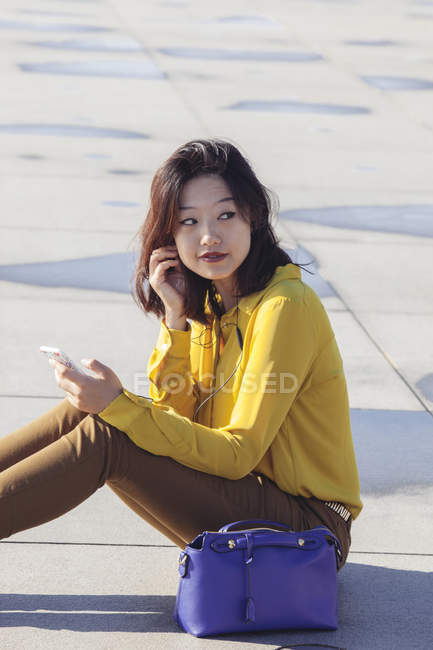 Весела молода китайська жінка сидить на підлозі слухаючи музику — стокове фото
