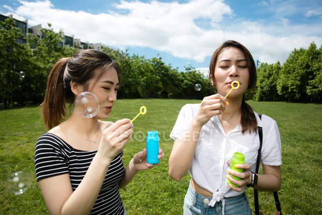 Lindo asiático novias haciendo jabón burbujas en el parque . - foto de stock