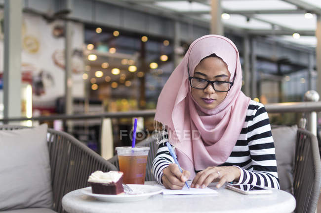Молодая женщина записывает некоторые сведения в кафе — стоковое фото