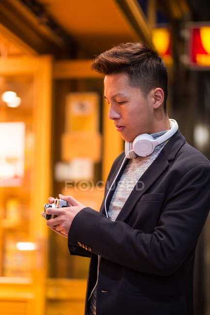 Casual joven chino merodeando por las calles de Madrid por la noche con cámara fotográfica, España - foto de stock