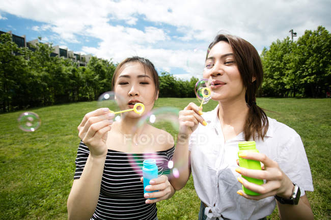 Cute asian girlfriends making soap bubbles in the park. — Stock Photo