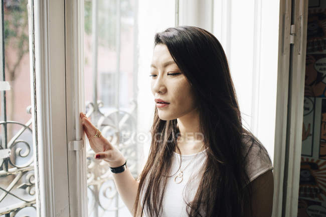 Atractivo asiático mujer buscando fuera de ventana - foto de stock